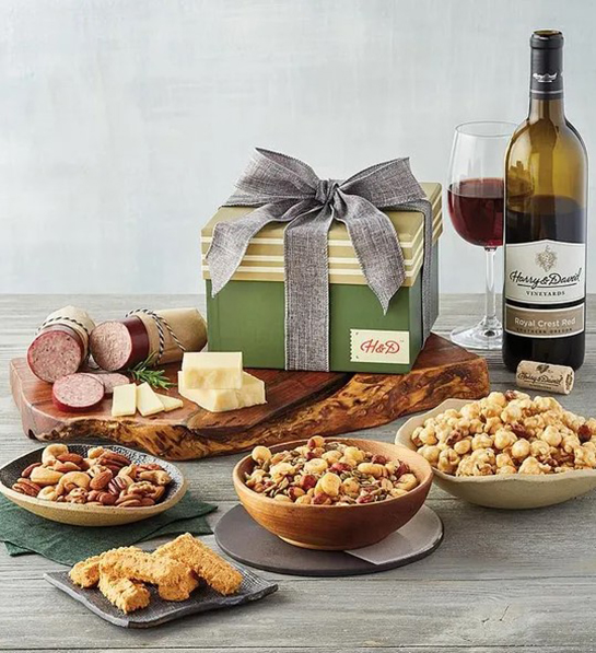 A photo of father's day gift ideas with a collection of bowls full of savory snacks next to a board full of salami and cheese with a bottle of wine