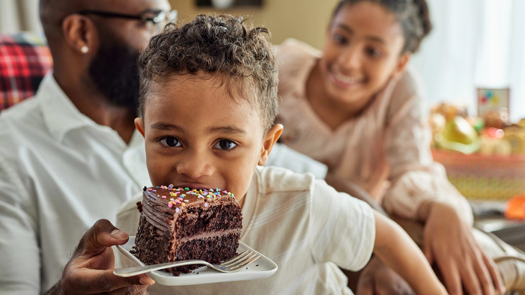 Food puns with a boy looking at the camera as he takes a bite out of a slice of chocolate cake.