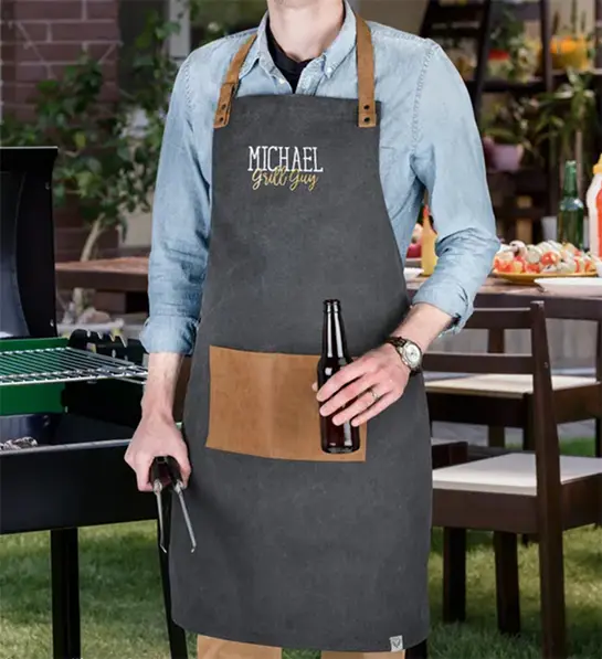 Photo of grilling gifts with a person wearing a personalized apron and holding tongs in one hand and a beer in the other.