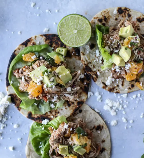 Photo of how to ripen an avocado with three open chicken tacos on a table.