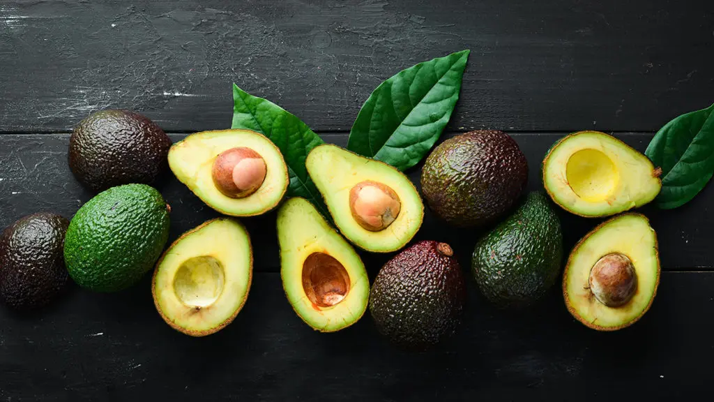 Photo of how to ripen an avocado with several avocados whole and cut in half on a table