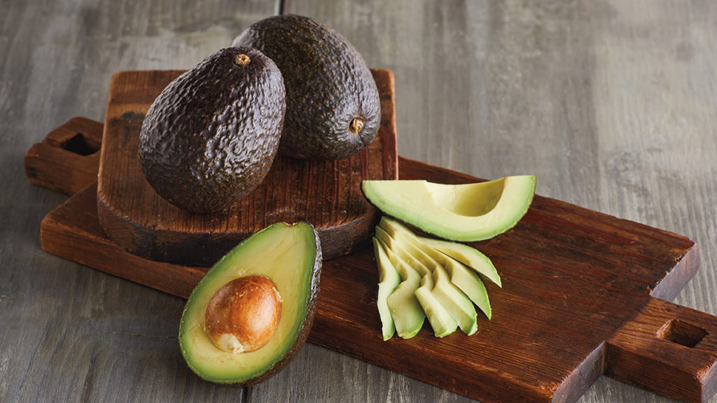 Photo of how to ripen an avocado with two whole avocados next to a sliced avocado, both on a wooden cutting board
