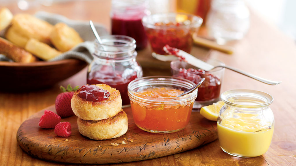 Photo of jelly vs jam with several pots of jam on a board next to English muffins