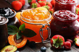 Photo of jelly vs jam with several small pots of jellies and jams surrounded by fruit.