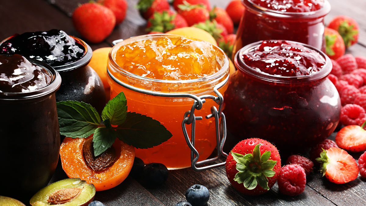 Photo of jelly vs jam with several small pots of jellies and jams surrounded by fruit.