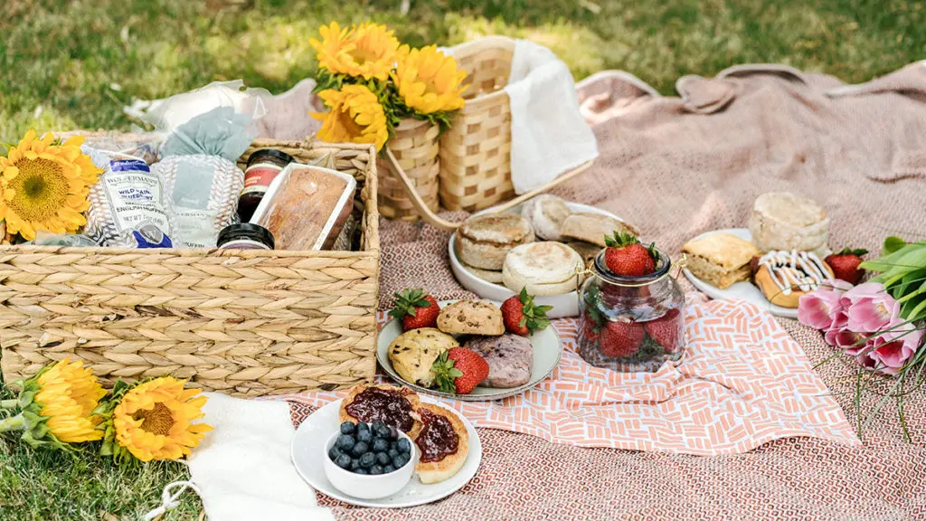 Photo of jelly vs jam with a picnic that has baskets full of Wolferman's English muffins, jams and jellies, flowers and more.