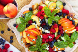 Photo of july recipes with a peach panzanella on a plate with whole peaches in a bowl next to it.
