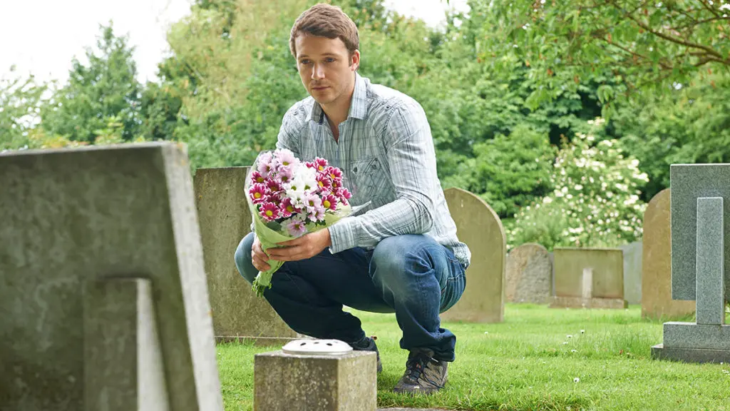 Photo of loss of dad on father's day with a man holding flowers while squatting next to a grave