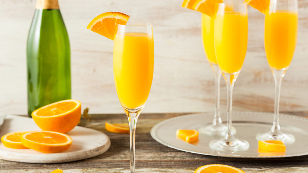 Photo of mimosa on a table surrounded by slices of oranges.