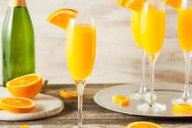 Photo of mimosa on a table surrounded by slices of oranges.