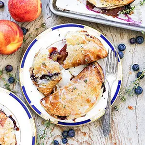 A photo of summer desserts with a plate of two blueberry and peach hand pies.