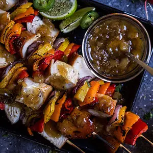 August recipes with a tray of teriyaki chicken skewers next to a bowl of charred pineapple relish.