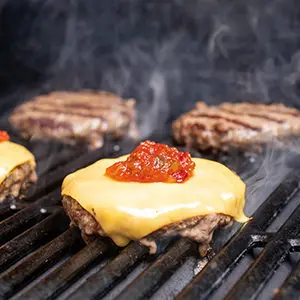 August recipes with four burgers on a grill two of them topped with cheese and relish