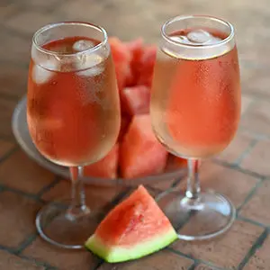 August recipes with two glasses of pink liquid next to a bowl of watermelon.
