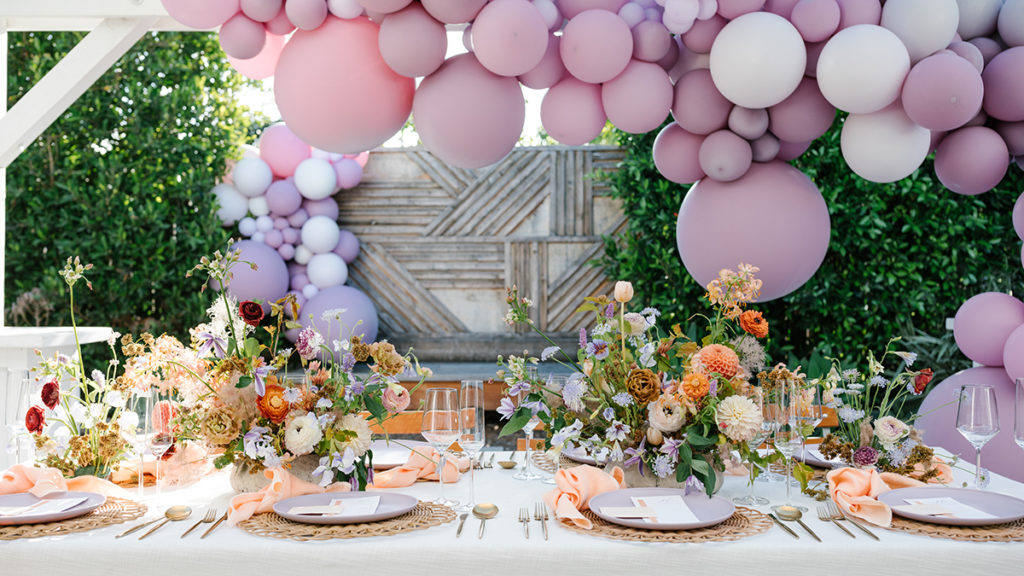 Bridal shower setup with balloon arch over a table full of flowers and set for dinner.