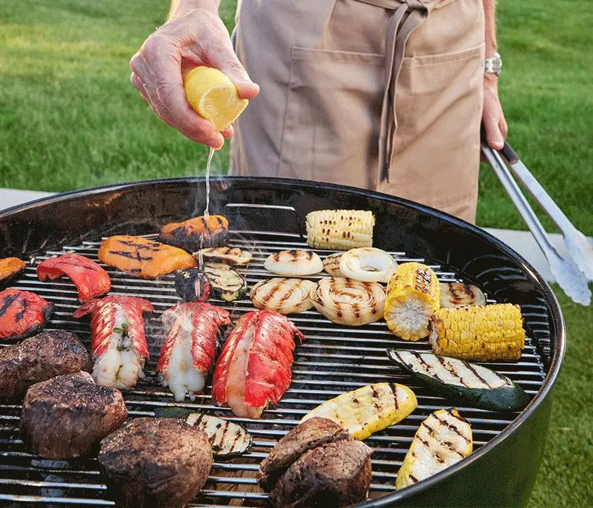 Photo of how to grill with a closeup of a grill full of meat, fish and vegetables with a hand squeezing lemon juice over it.