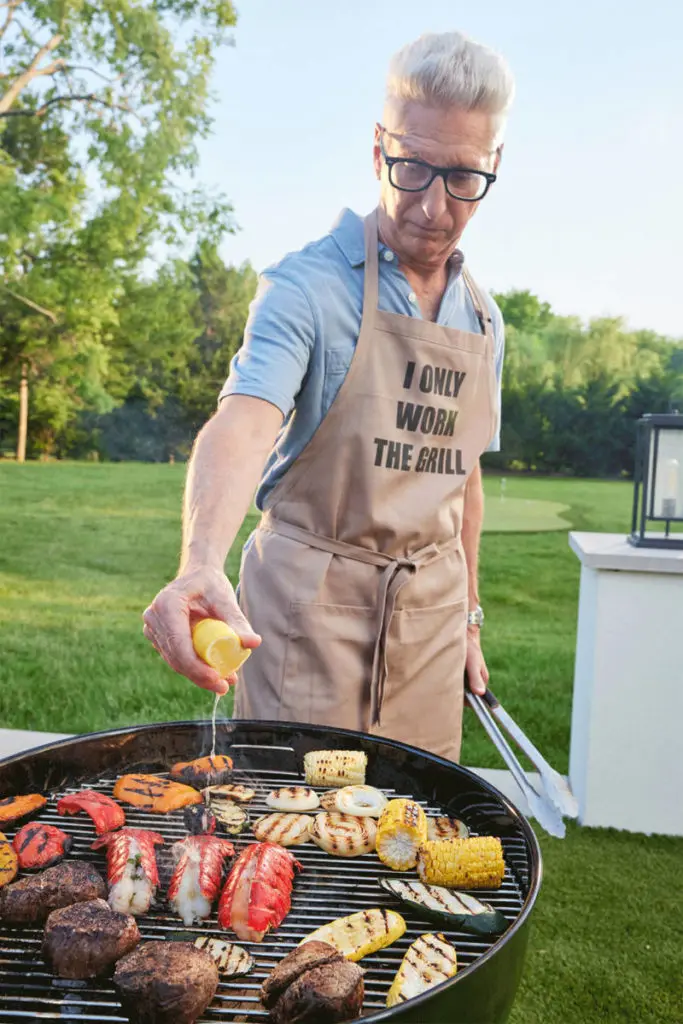 Photo of how to grill with a man working over a grill full of meat, fish and vegetables.