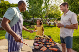 Photo of how to grill with two men standing at a grill smiling at a young girl.