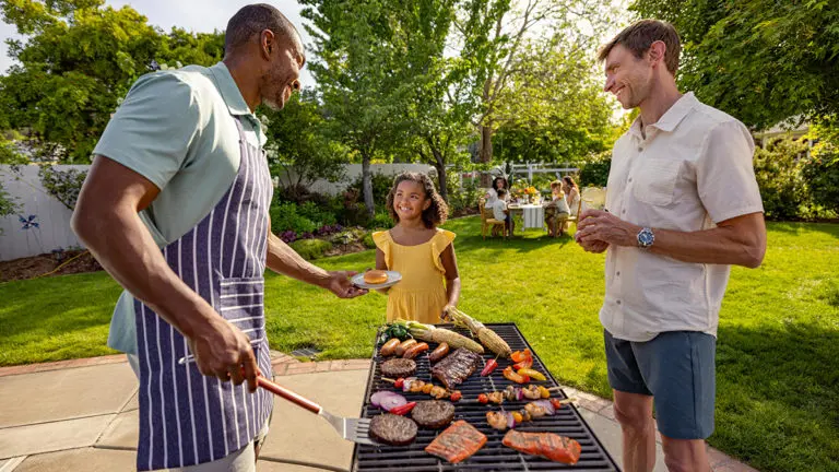 Photo of how to grill with two men standing at a grill smiling at a young girl.