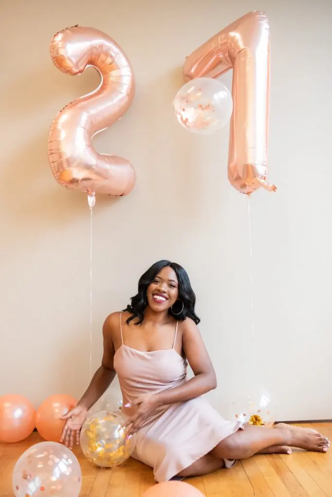 Party themes for adults with a woman sitting underneath balloons that say 21.