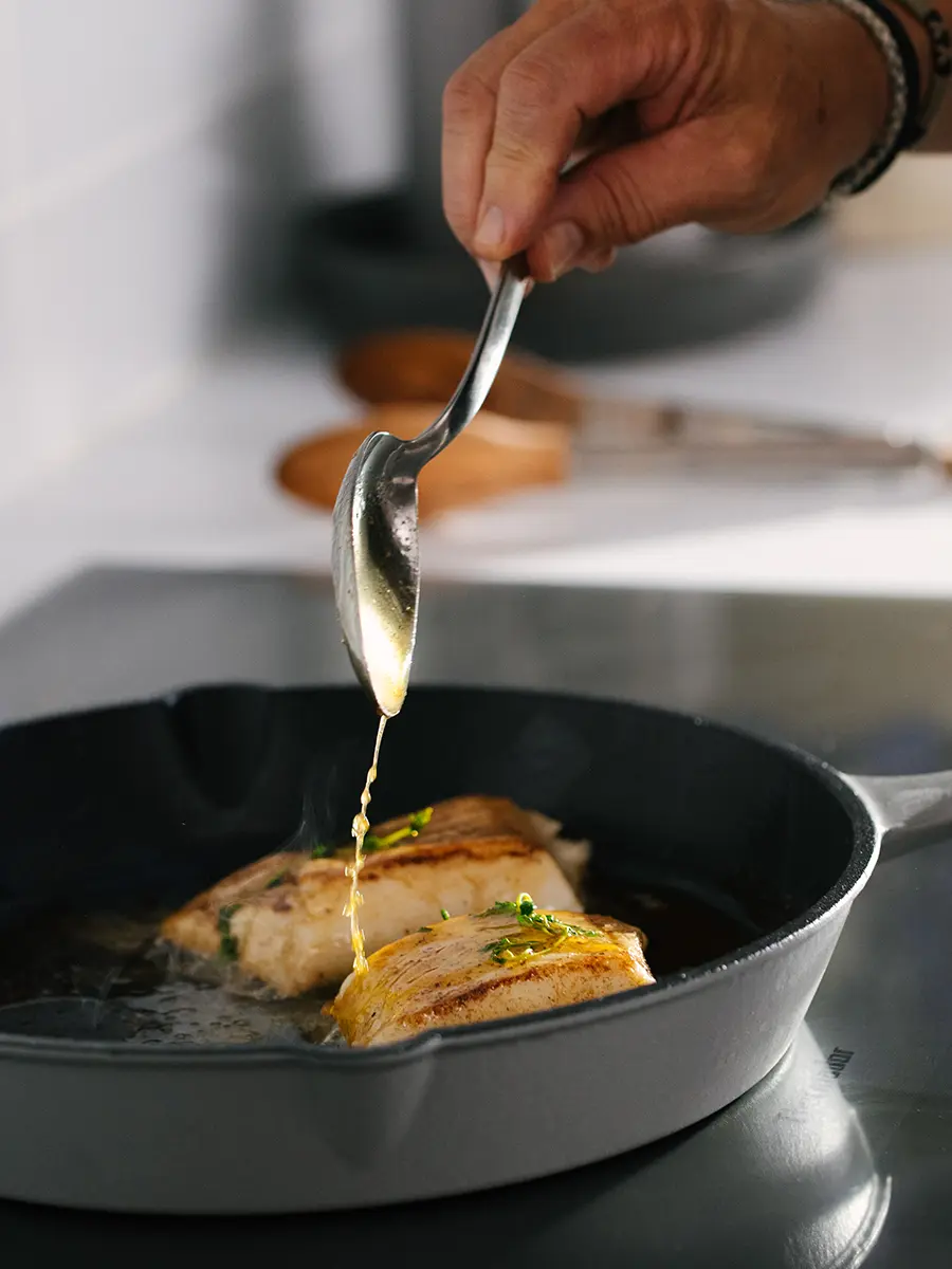 Sea bass being basted in a cast iron skillet.