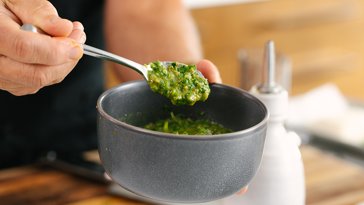 Sea bass with a hand spooning out caper mint relish from a bowl.