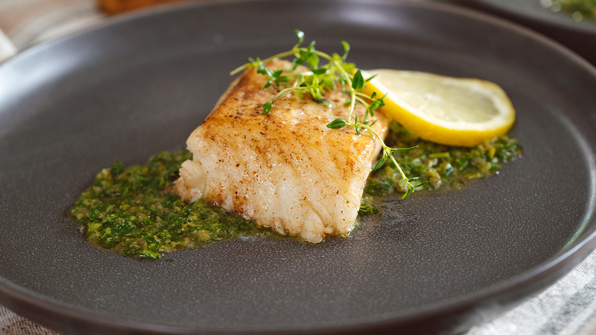 Sea bass on a plate with mint caper relish, a sprig of thyme and a slice of lemon.