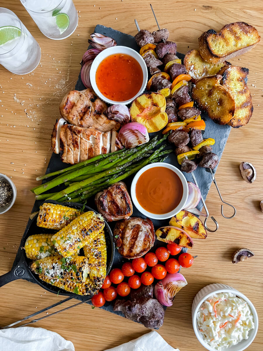 Snack board ideas with a board full of grilled meat, vegetables and sauces.