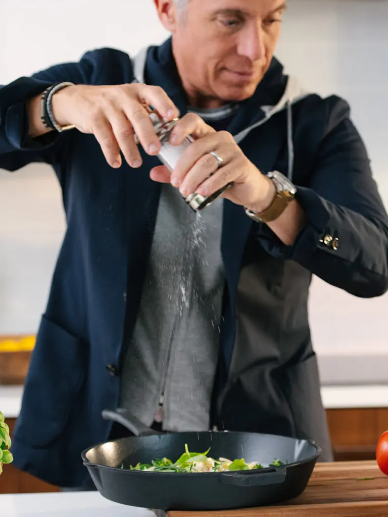 Chef geoffrey zakarian seasoning food in an iron skillet.