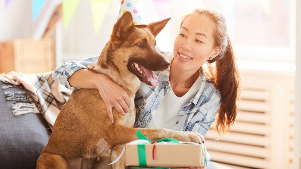 Gifts for pets with a woman holding a present sitting next to a dog.