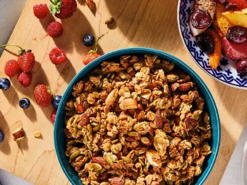 Granola in a bowl surrounded by bowls of fruit.