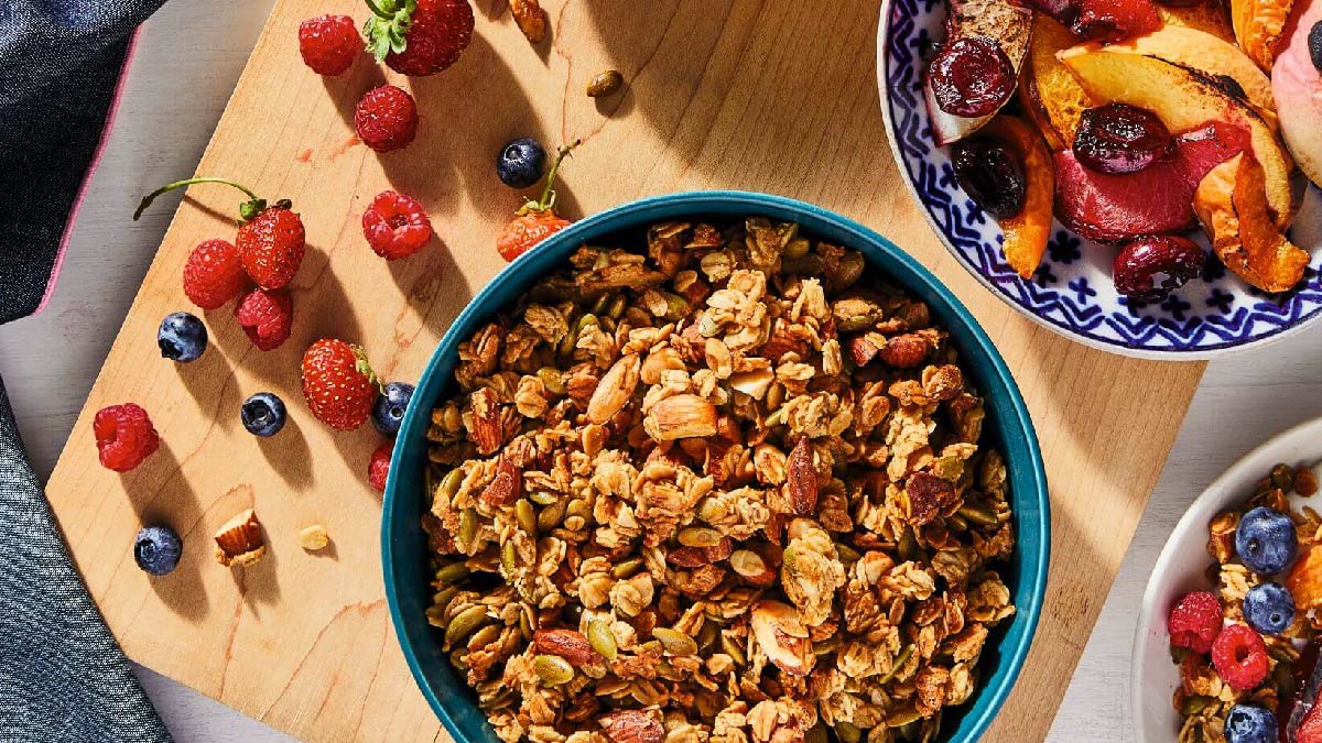 Granola in a bowl surrounded by bowls of fruit.