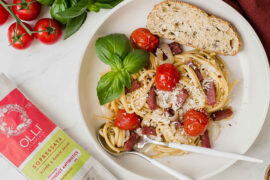 September recipes with a bowl full of salami pasta and tomatoes with a sprig of basil and a slice of bread.