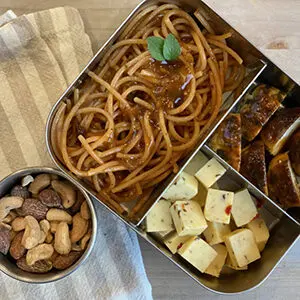 September recipes with a lunch box full of spaghetti, meatballs and cubes of cheese next to a small ramekin of mixed nuts.