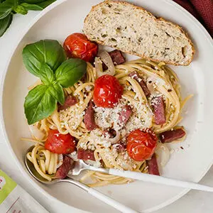 September recipes with a bowl full of salami pasta and tomatoes with a sprig of basil and a slice of bread.