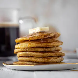 September recipes with a stack of pumpkin pancakes on a plate topped with a slice of butter and maple syrup.
