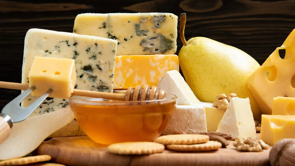 Types of cheese on a board with crackers, honey and a pear.