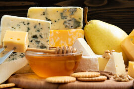 Types of cheese on a board with crackers, honey and a pear.