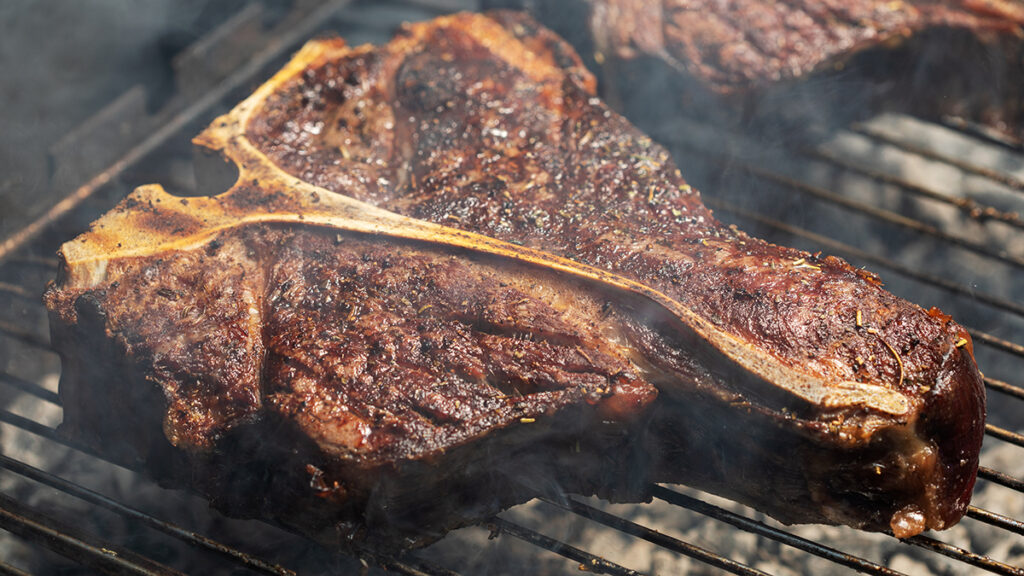 Wines for tailgating with a porterhouse steak on a grill.