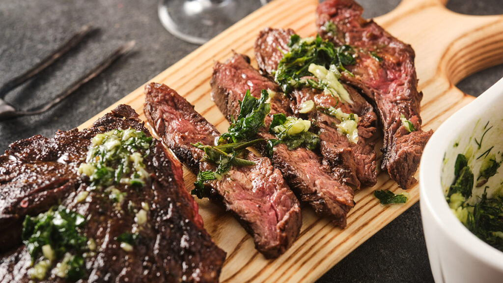 Wines for tailgating with slices for skirt steak on a cutting board with chimichurri on top.