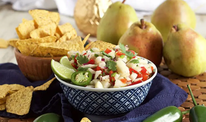 Pear salsa in a bowl surrounded by whole pears and tortilla chips