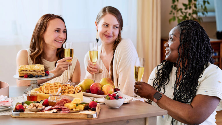 Birthday party food ideas with three women drinking champagne and eating brunch.