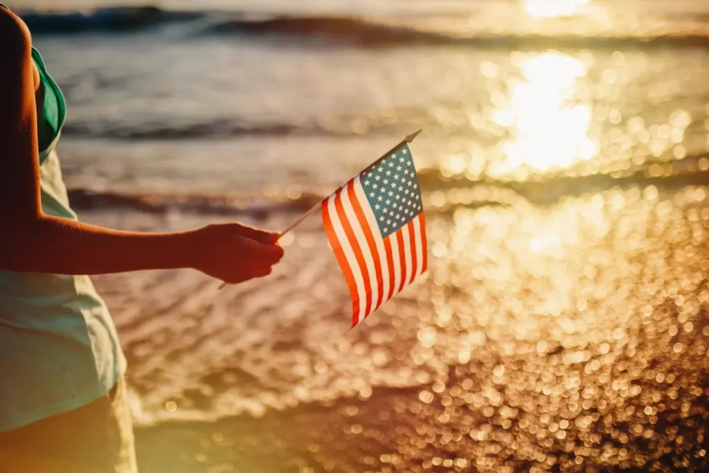 Celebrating workers on labor day, someone holds an American flag by the beach