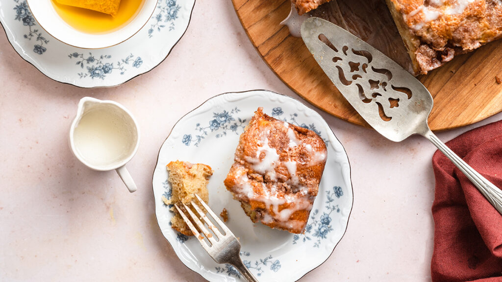 Cinnamon apple cake on a plate next to a cup of tea.