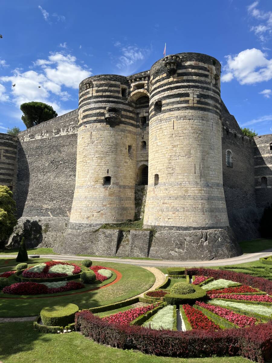 A view of the Chateau d'Angers, and two of its 17 towers made of slate and limestone, overlooking the manicured gardens.