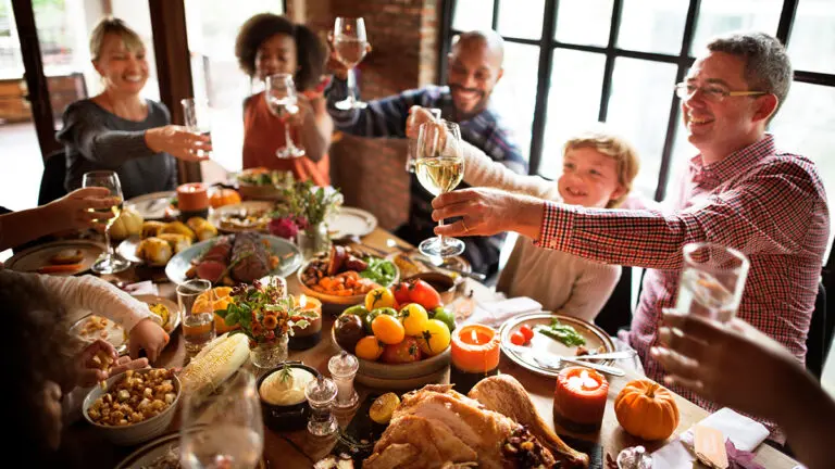 Fall birthday party with a group of people clinking glasses while sitting at a table full of food.