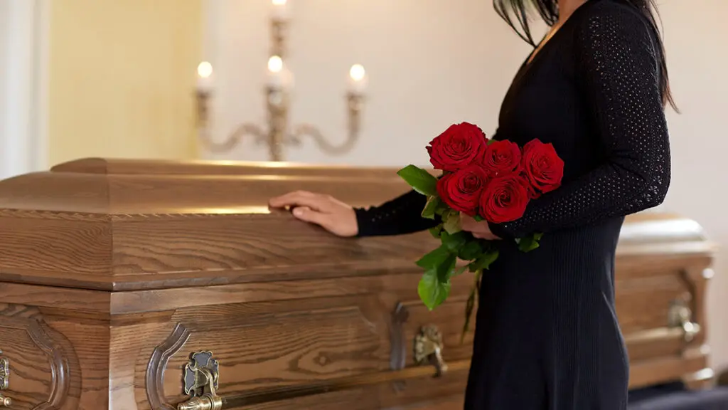 Funeral etiquette with a woman touching a coffin while holding a bouquet of roses.