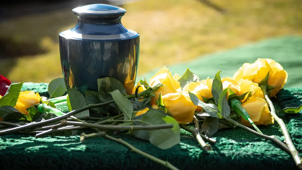 Funeral etiquette with an urn on a table surrounded by yellow roses.