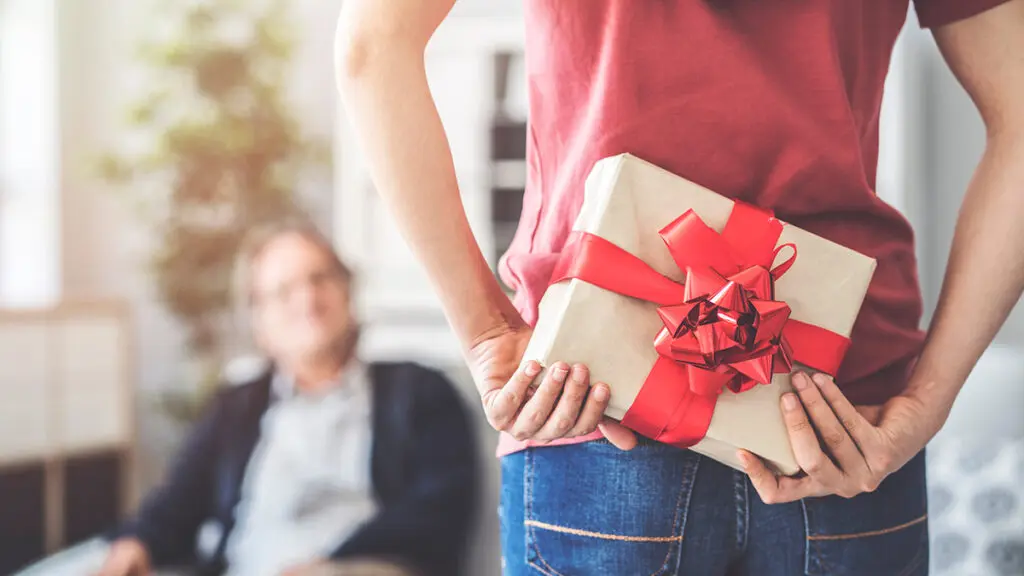 Giving a gift to a father with the daughter holding it behind her back.