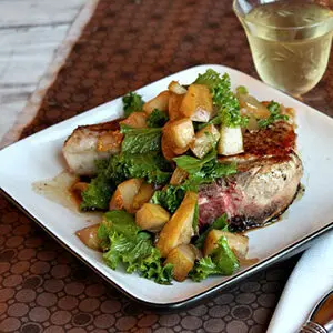 Pear recipes with a pork chop on a plate covered with pears and greens.